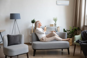 Woman sits on couch using remote control on ductless unit