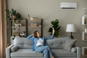 woman lounges on couch and adjusts ductless HVAC system